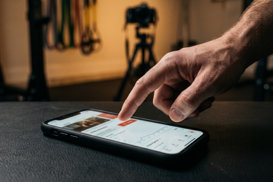 Fitness coach reviewing published workout tutorial analytics on a smartphone showing views and engagement metrics